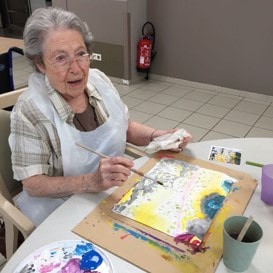 Résident senior peignant dans un atelier artistique d’une maison de repos en Belgique, illustrant les activités proposées lors d’une visite.
