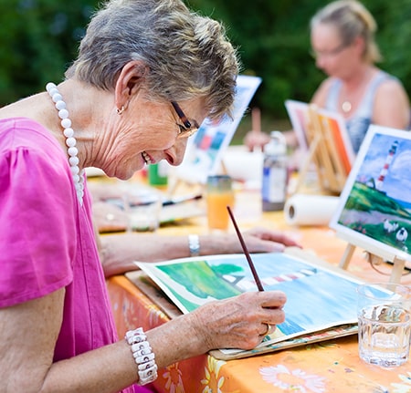 Personne âgée participant à une activité de peinture en maison de repos, illustrant les bienfaits des thérapies non médicamenteuses pour les seniors.